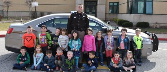 Sheriff with children in front of vehicle.