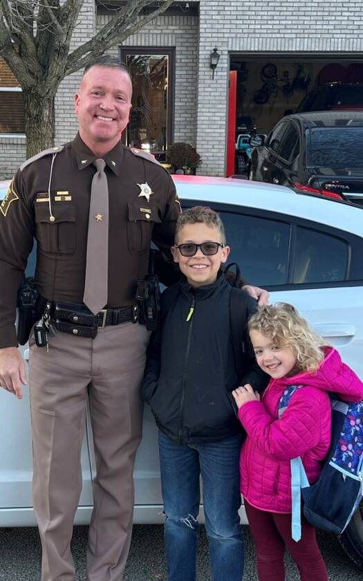 Officer with two young children next to a sheriff's car.